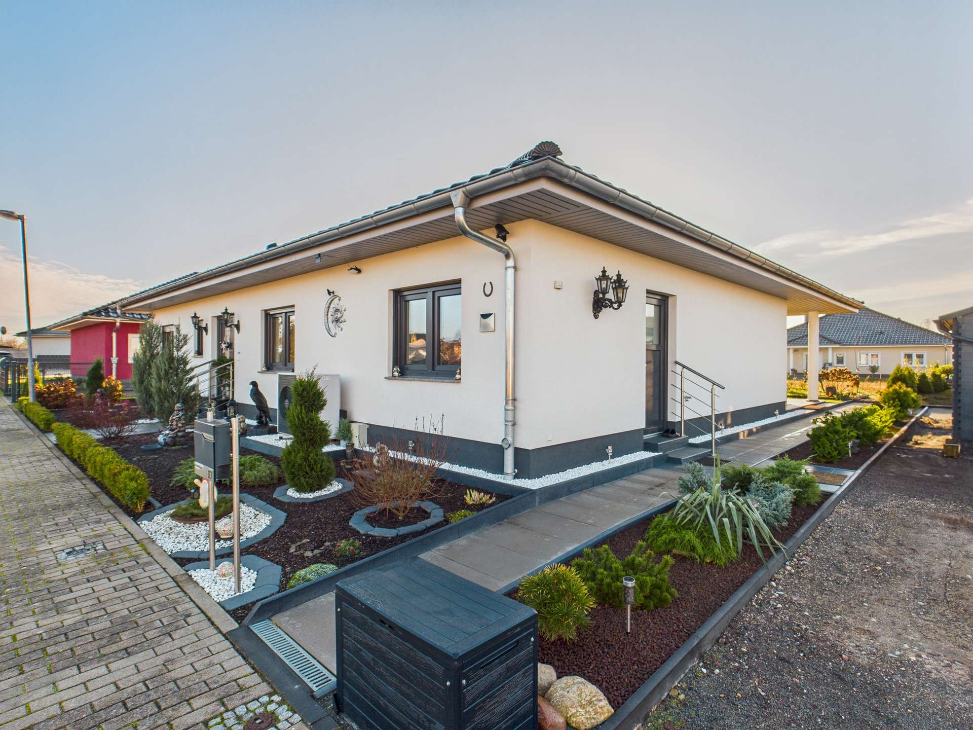 Ein modernes Einfamilienhaus mit gepflegtem Vorgarten und Steinwegen, umgeben von Bepflanzungen.