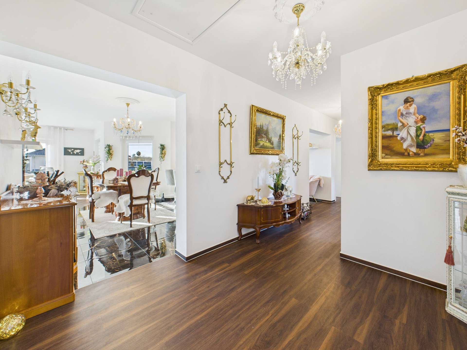 Eleganter Flur mit Holzboden, Kronleuchtern und Kunstwerken, der zu einem stilvollen Essbereich führt.