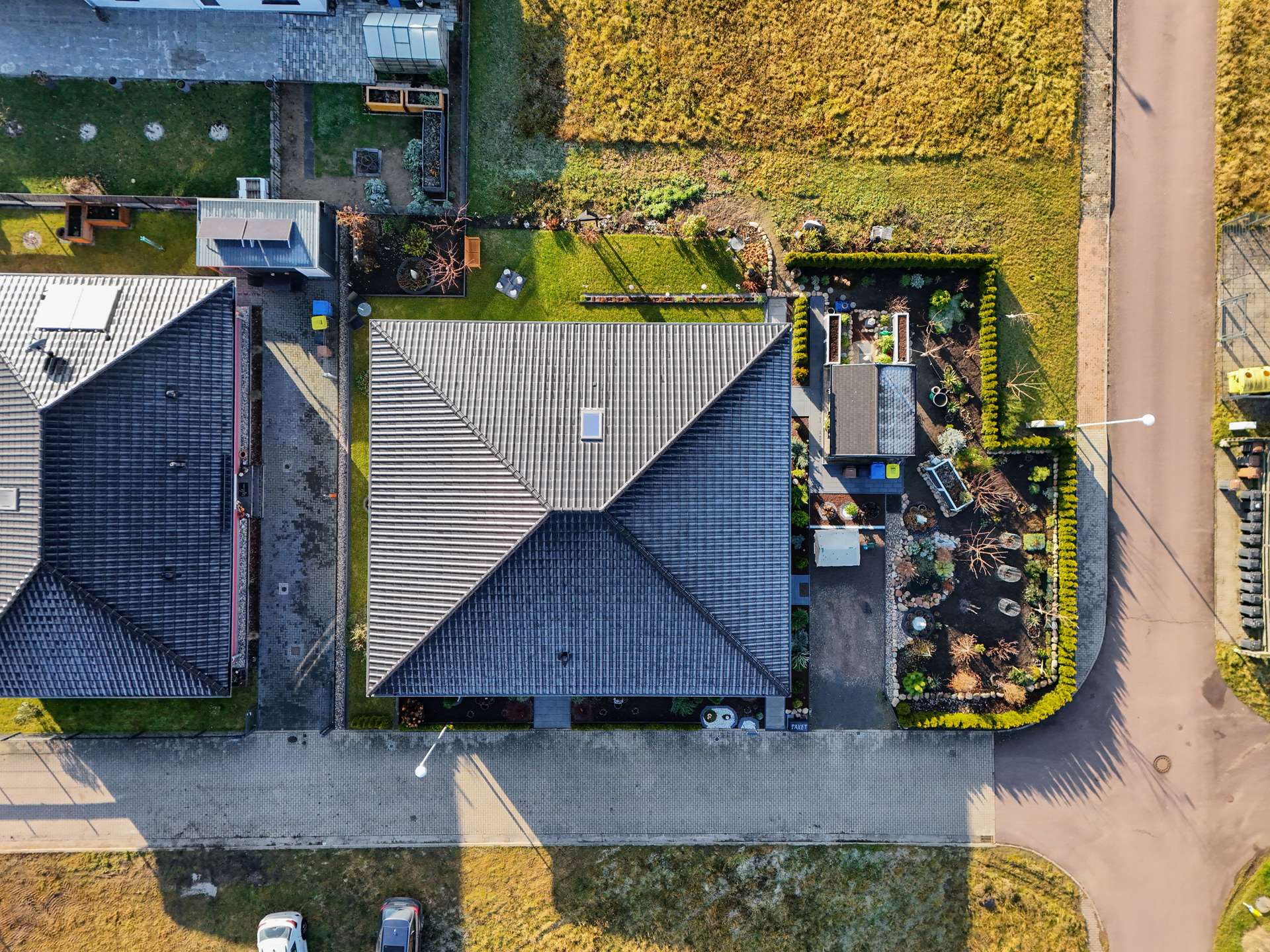 Luftaufnahme eines Wohnhauses mit Garten und Nachbarhäusern, umgeben von Rasen und gepflasterter Straße.