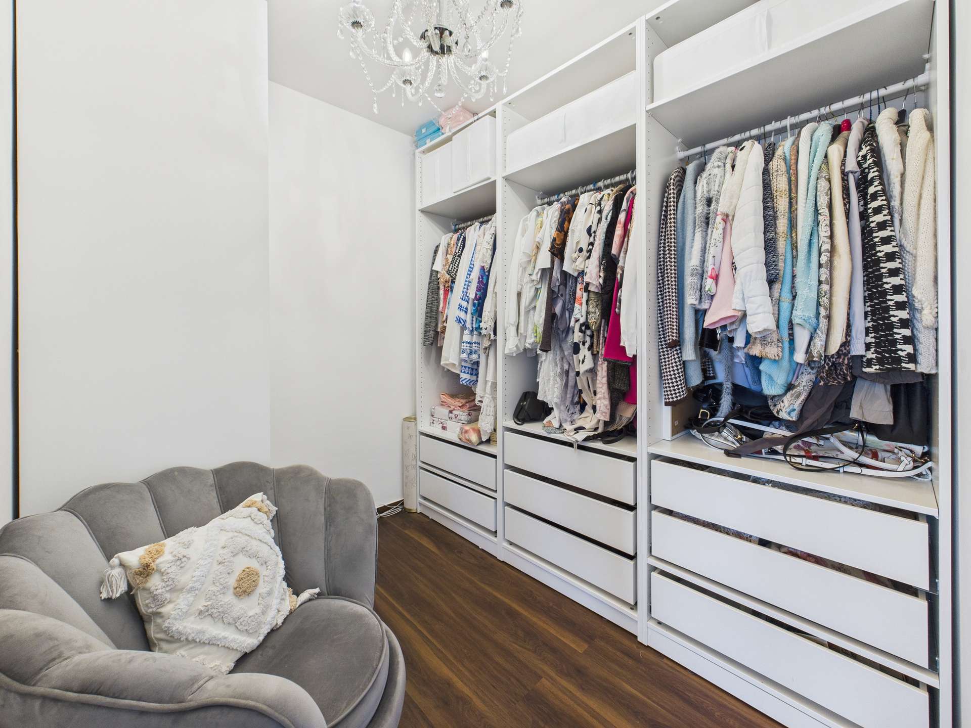 Ein moderner Kleiderschrank mit ordentlichen Regalen, gefüllt mit Kleidung, und einem stilvollen Sessel im Vordergrund.