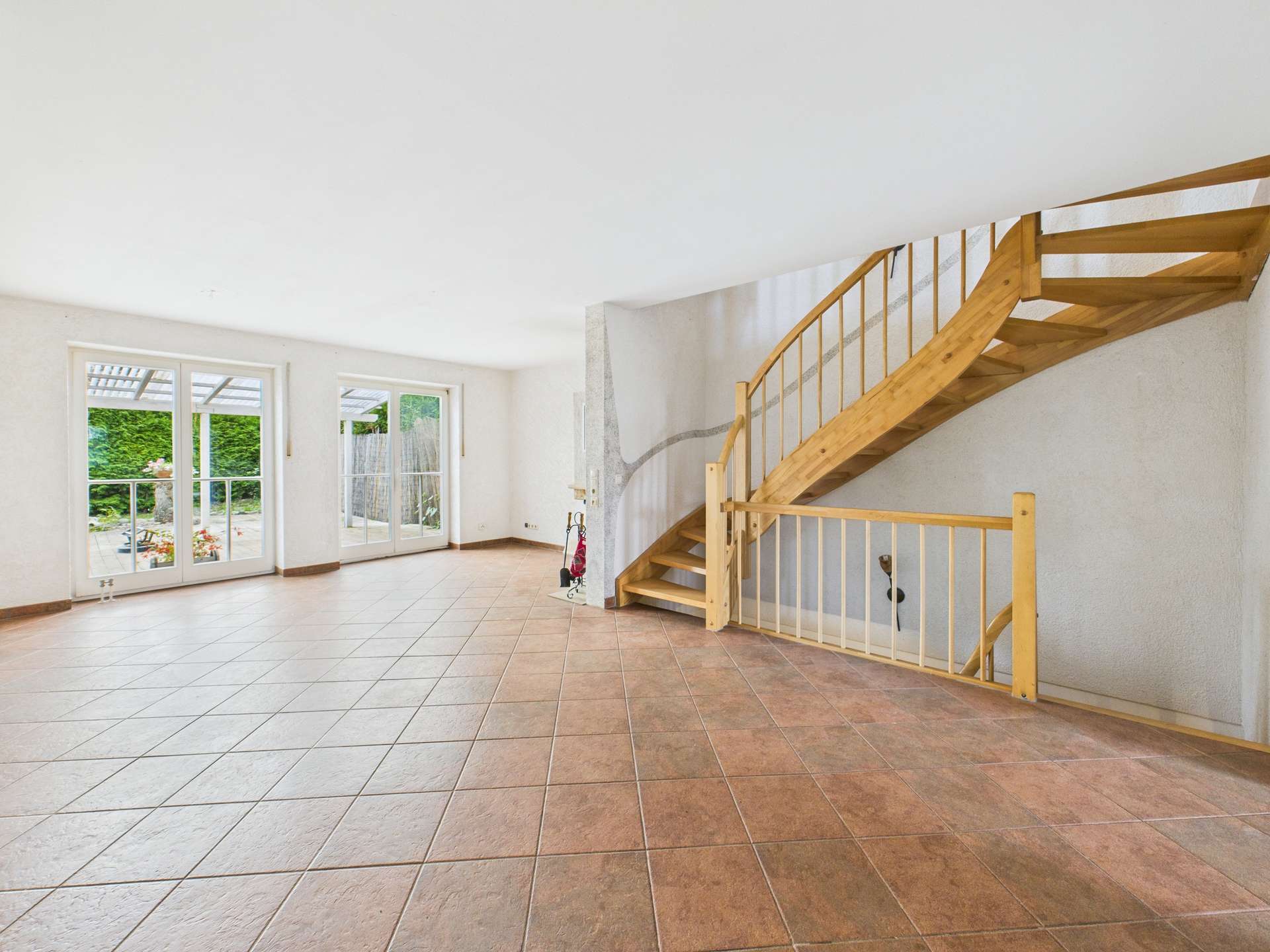 Helles, offenes Wohnambiente mit Fliesenboden und Holztreppe, große Fenster mit Blick auf den Garten.