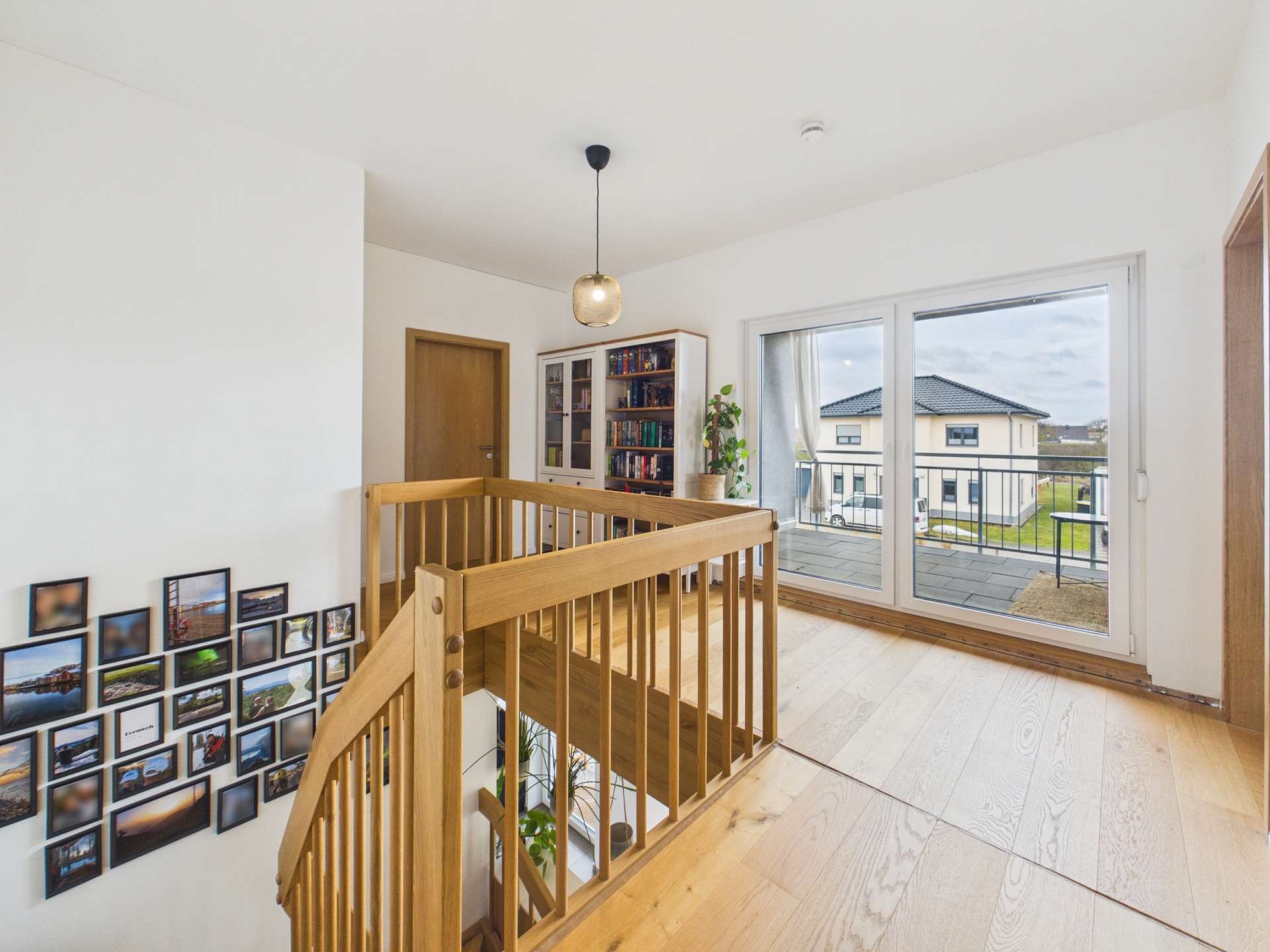 Heller Flur mit Holztreppe, Bücherregal und Fenster zur Terrasse, geschmückt mit Fotowand.