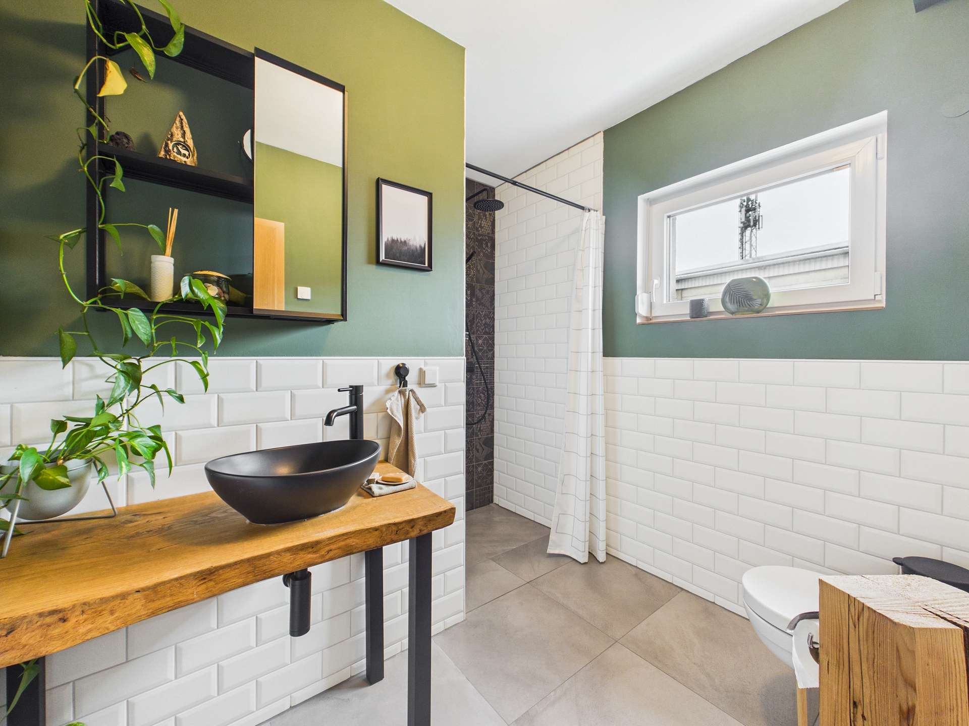 Modernes Badezimmer mit grünem Akzent, Holzwaschtisch, schwarzem Waschbecken und Dusche mit Glasabtrennung.