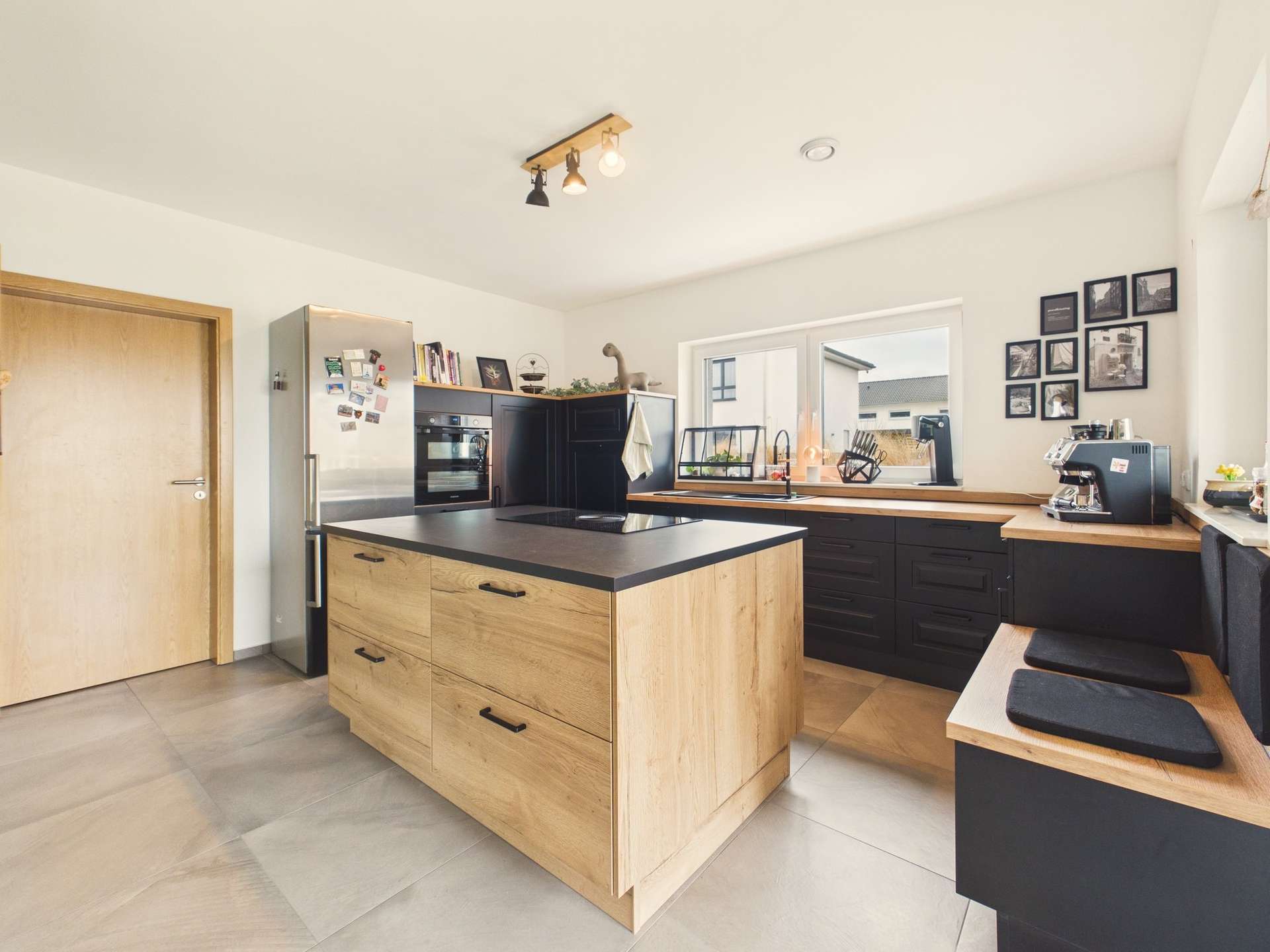 Moderne Küche mit Holz- und schwarzen Elemente, zentraler Kücheninsel und großen Fenstern für viel Licht.