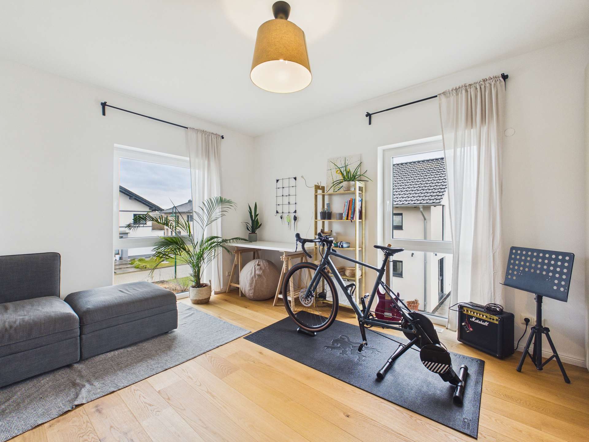 Heller Raum mit einem Sofa, einem Schreibtisch, einer Pflanze und einem Fitness-Bike auf einem schwarzen Untergrund.