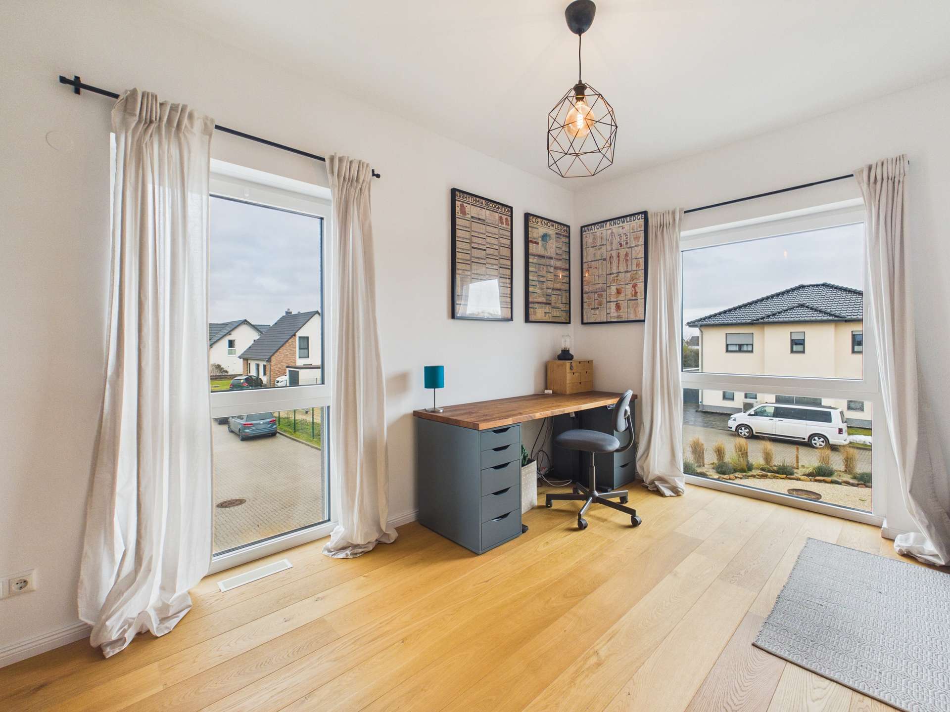 Ein helles Arbeitszimmer mit Schreibtisch, Stuhl und großen Fenstern, die auf eine ruhige Wohnstraße blicken.