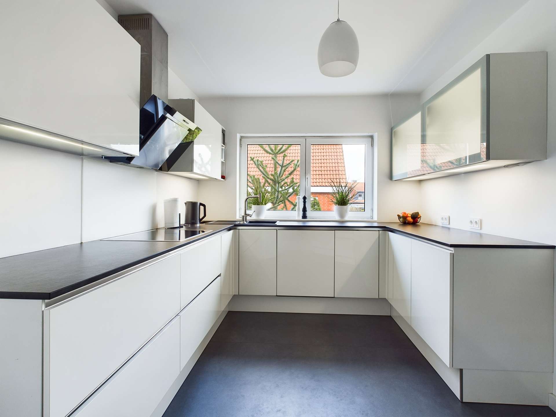Moderne, helle Küche mit weißen Schränken, schwarzer Arbeitsplatte und großen Fenstern.