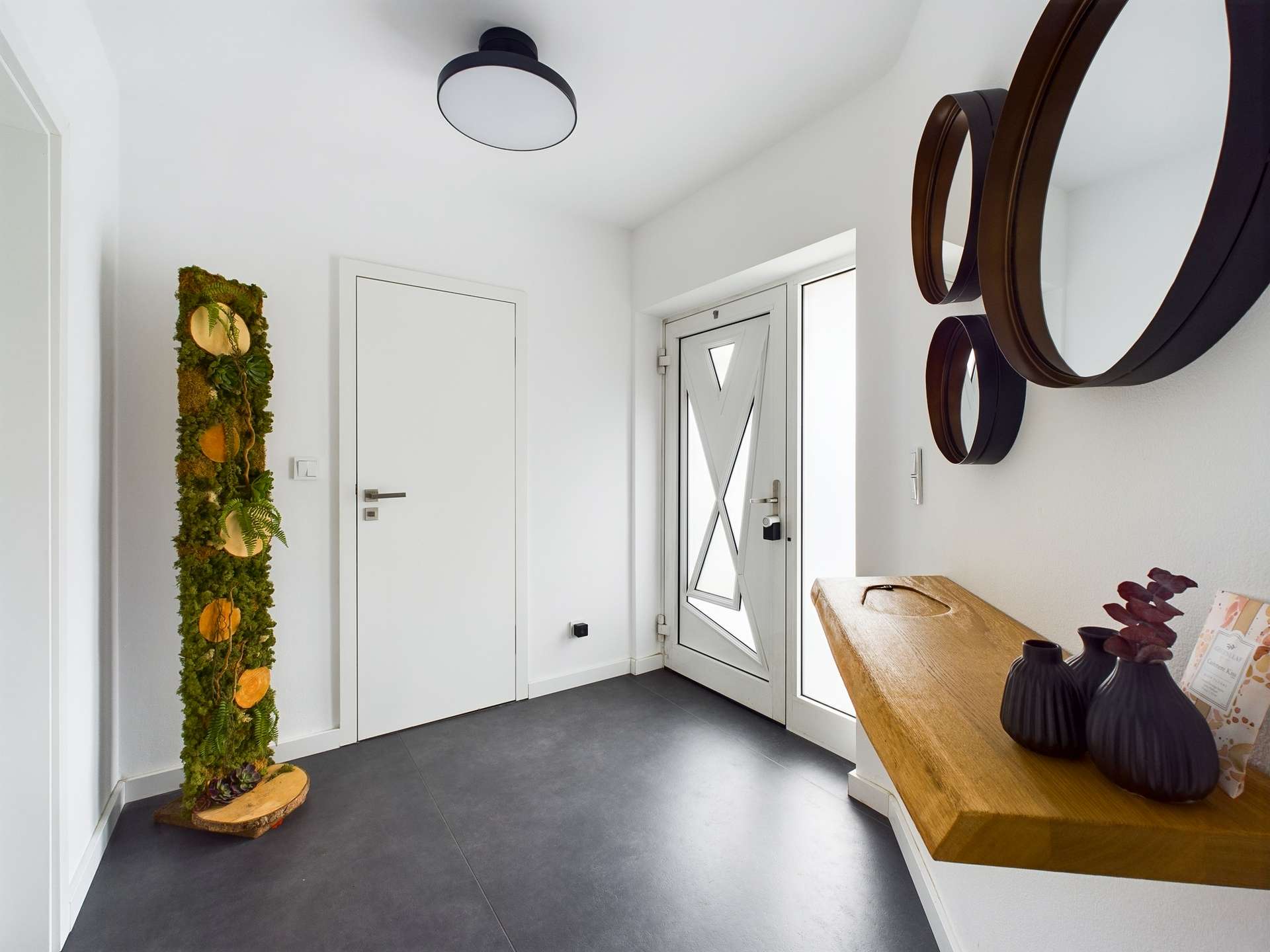 Ein moderner Flur mit einer grünen Wanddekoration, minimalistischer Holzablage und eleganten Spiegeln.