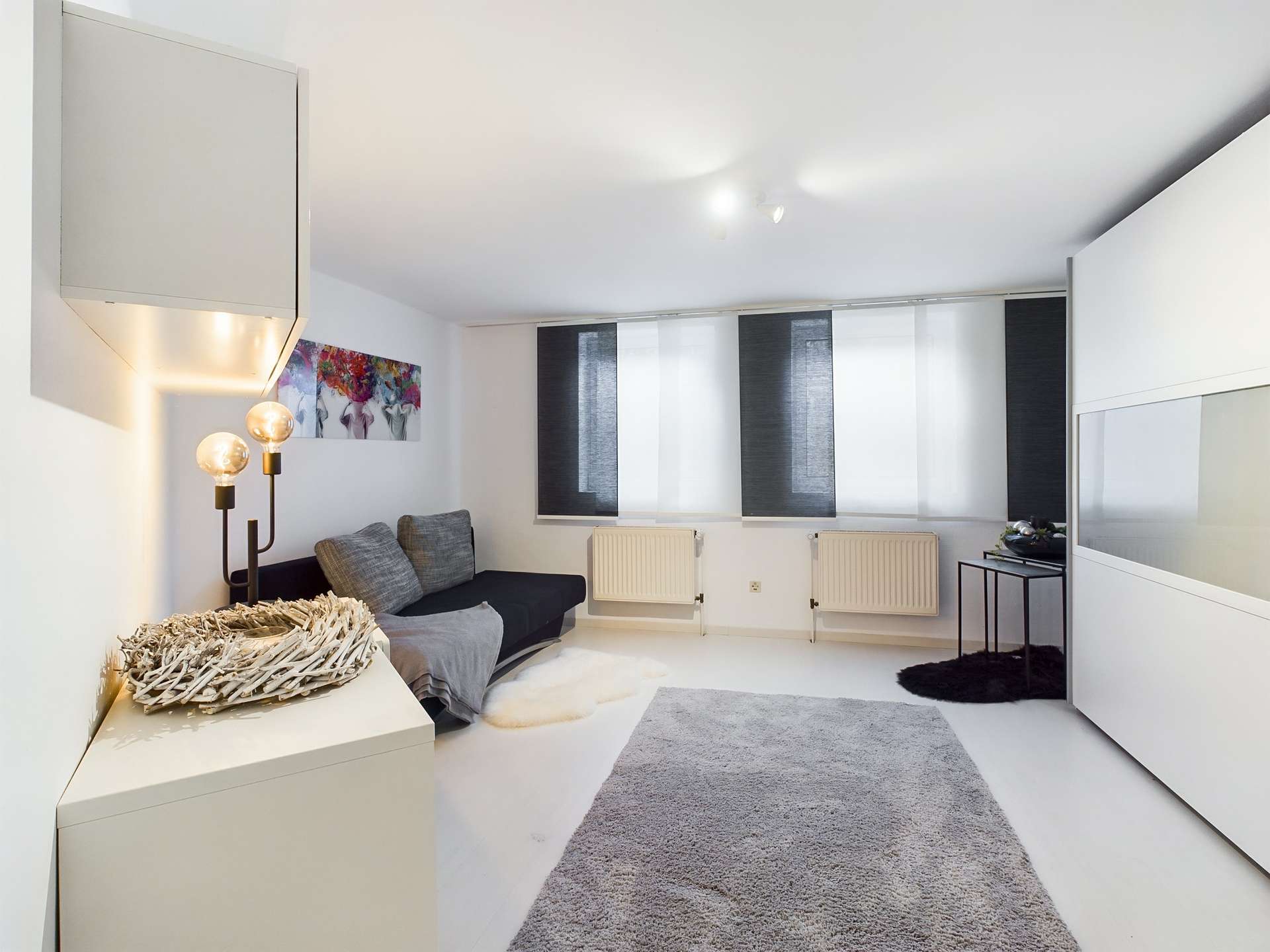 Moderne, minimalistische Wohnraum mit Sofa, Teppich und großen Fenstern, die für viel Licht sorgen.