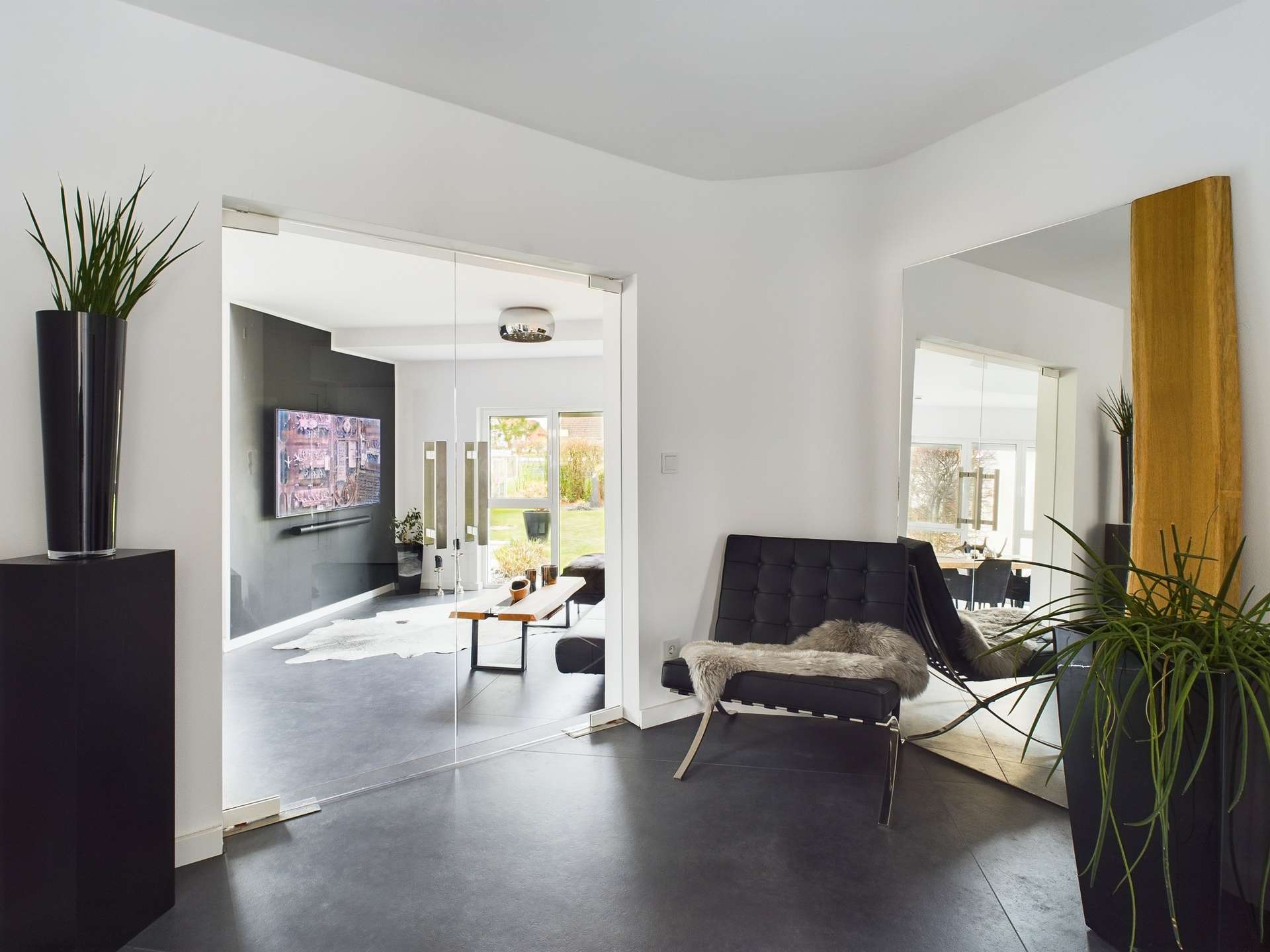 Modernes Wohnzimmer mit schwarzer Wand, Glaswand, Pflanzen und stilvollem Mobiliar.