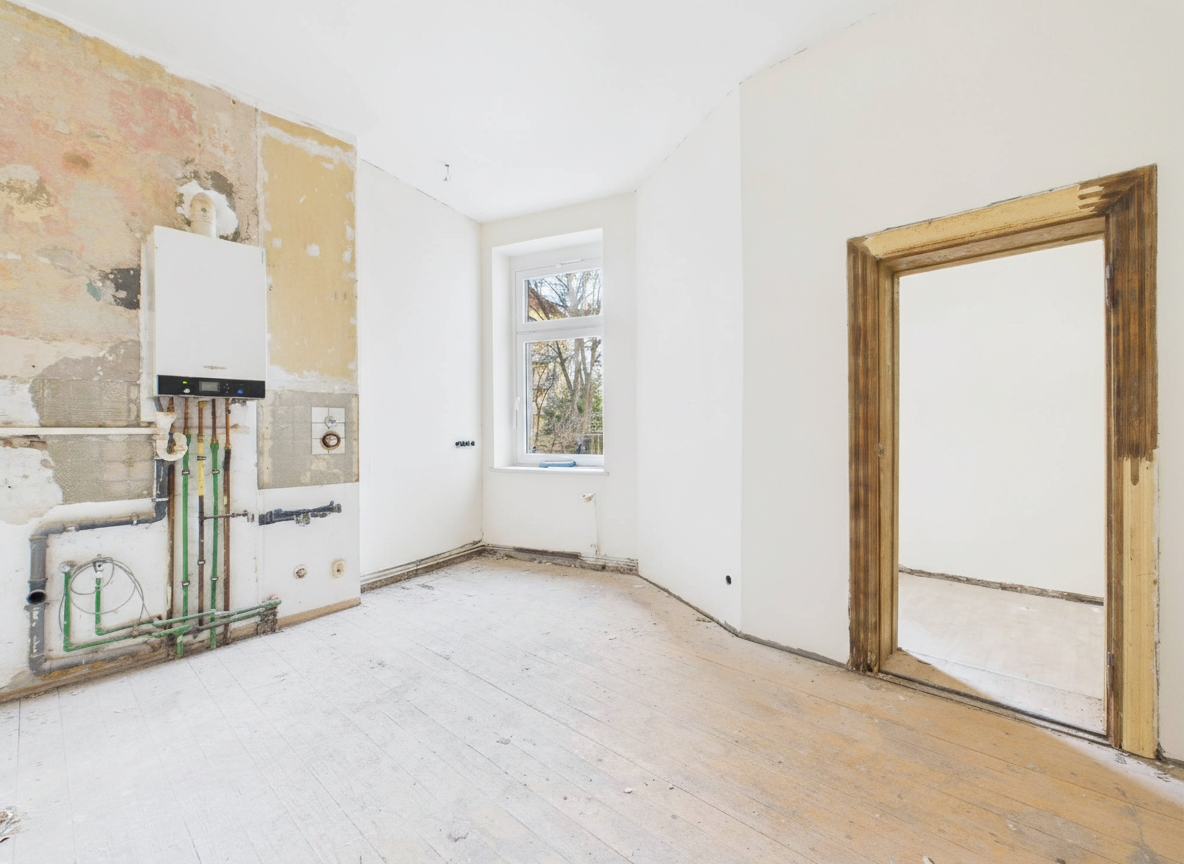 Leere, renovierungsbedürftige Zimmer mit freiliegenden Rohren und Fenster, die auf einen Gartenblick zeigen.