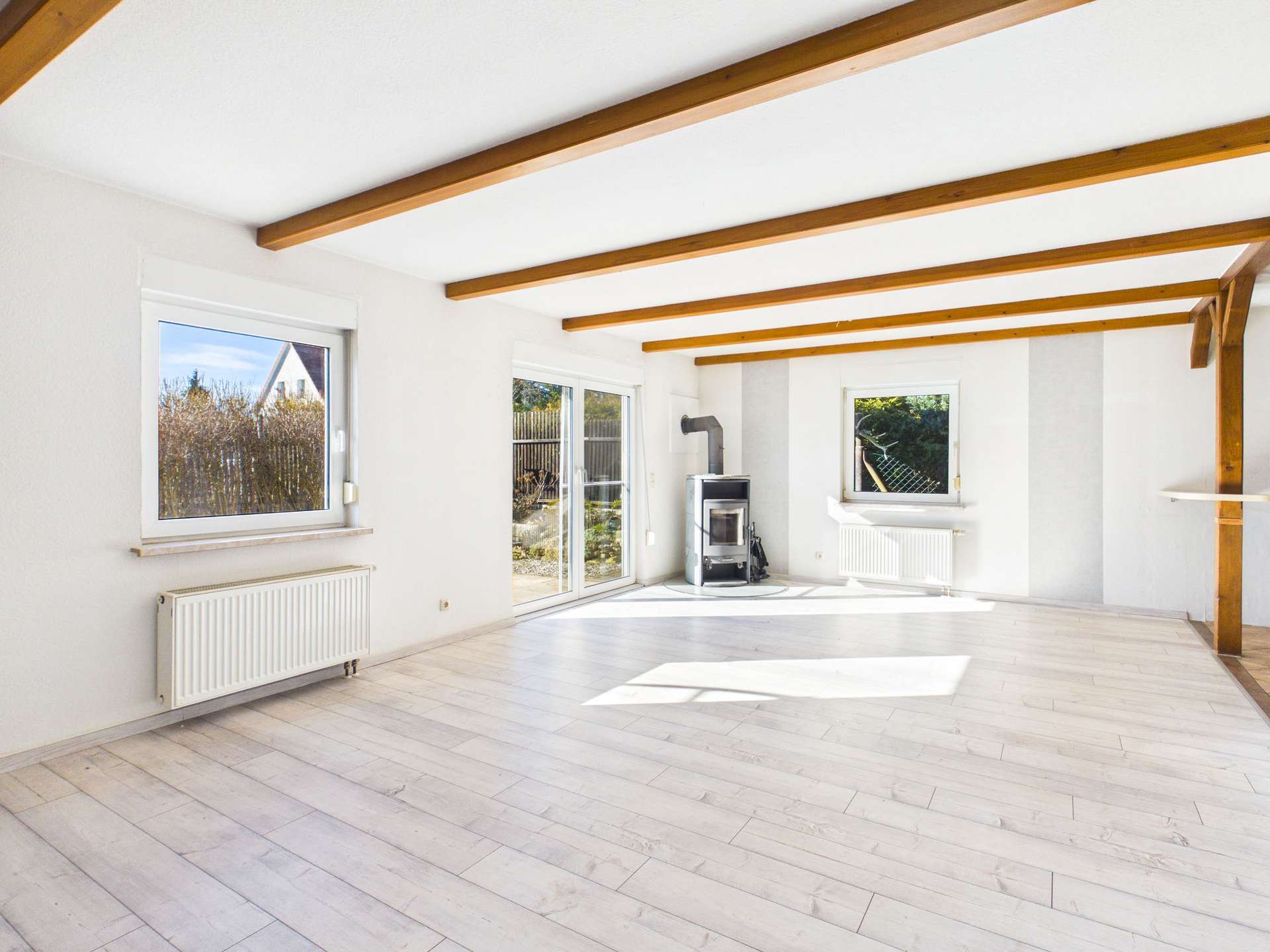 Helles Wohnzimmer mit Holzbalken, großen Fenstern und einem Kamin, auf hellem Boden in modernem Stil.