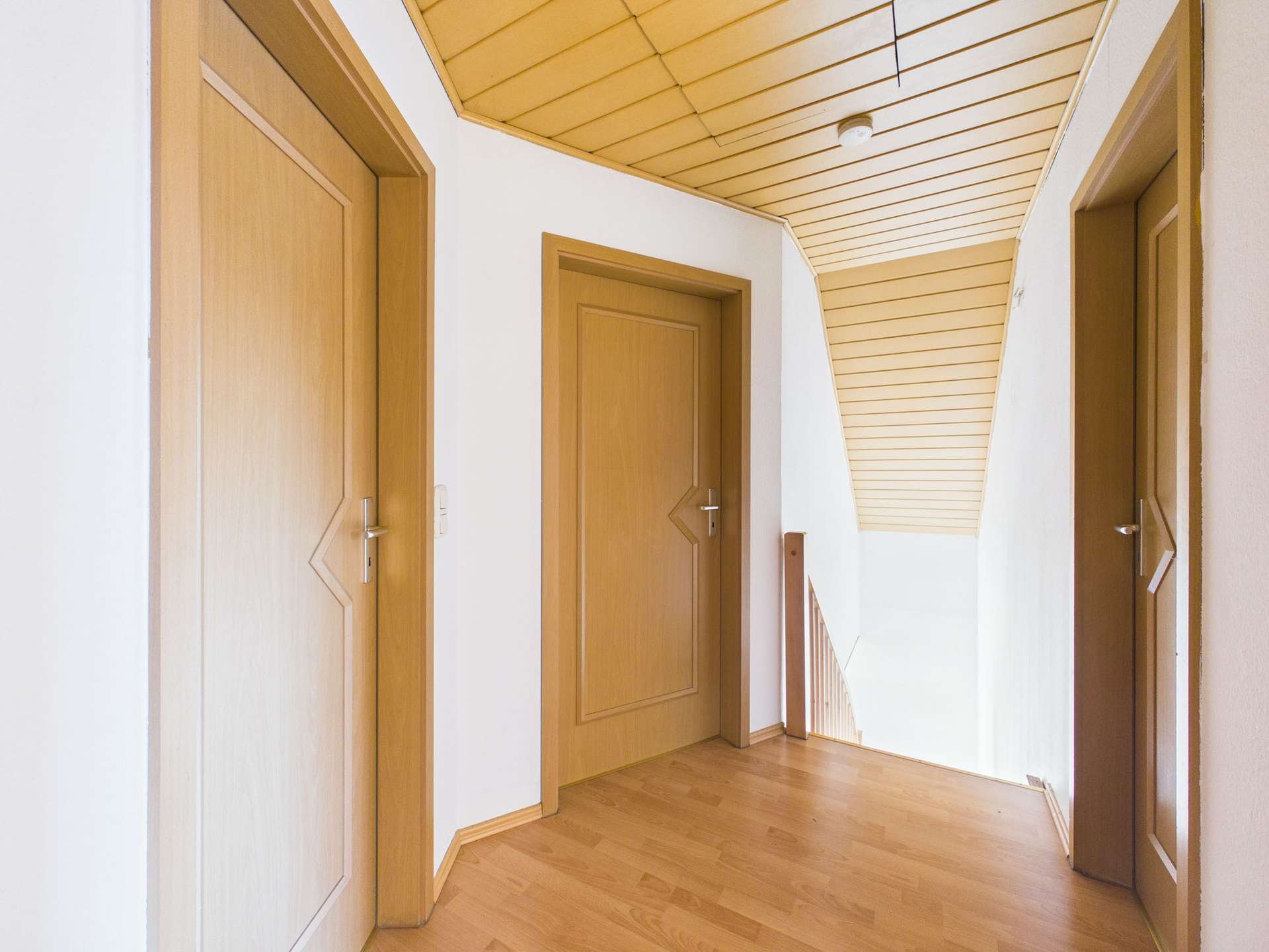 Flur mit zwei Holz-Türen und einer Treppe, helle Wände und Holzdecke, minimalistische Gestaltung.