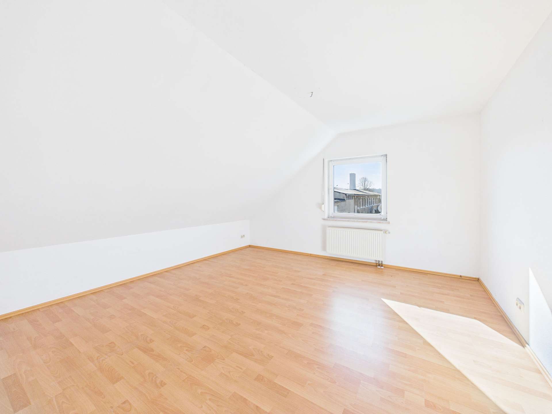 Helle, leere Dachzimmer mit Holzfußboden und Fenster, das Tageslicht hereinlässt.