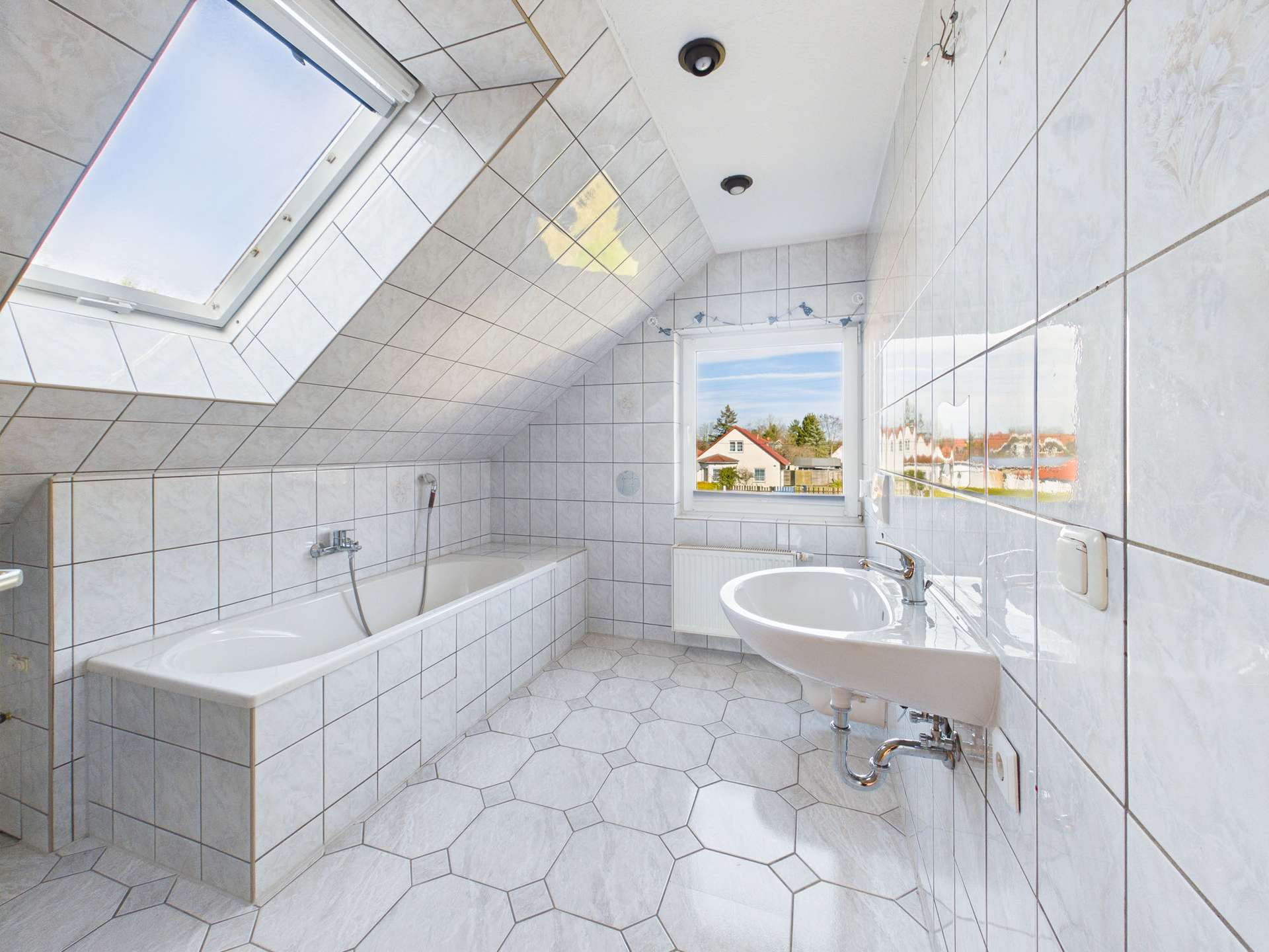 Helles Badezimmer mit Dachschräge, Badewanne, Waschbecken und Fenster mit Blick auf die Landschaft.