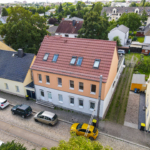 Luftaufnahme eines Wohngebiets mit einem orangefarbenen Gebäude, gepflasterter Straße und geparkten Autos.