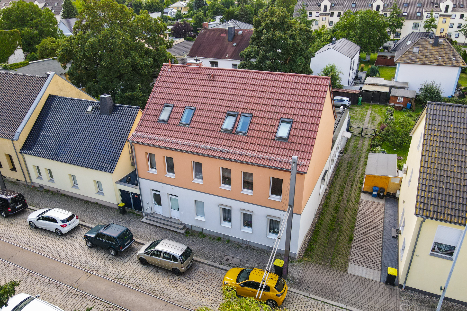 Luftaufnahme eines Wohngebiets mit einem orangefarbenen Gebäude, gepflasterter Straße und geparkten Autos.