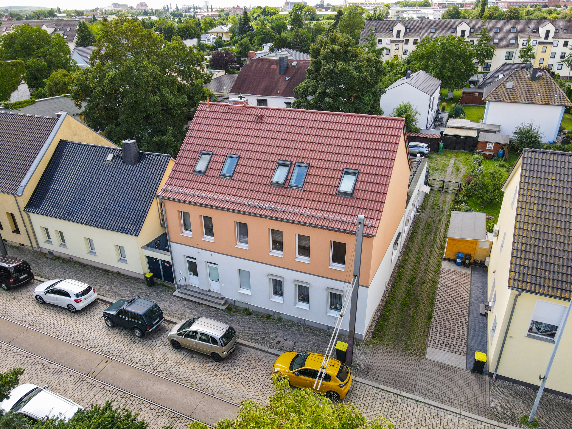 Luftaufnahme eines Wohngebiets mit einem orangefarbenen Gebäude, gepflasterter Straße und geparkten Autos.