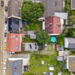 Luftaufnahme eines Wohngebiets mit Häusern, Gärten und geparkten Autos auf der Straße.