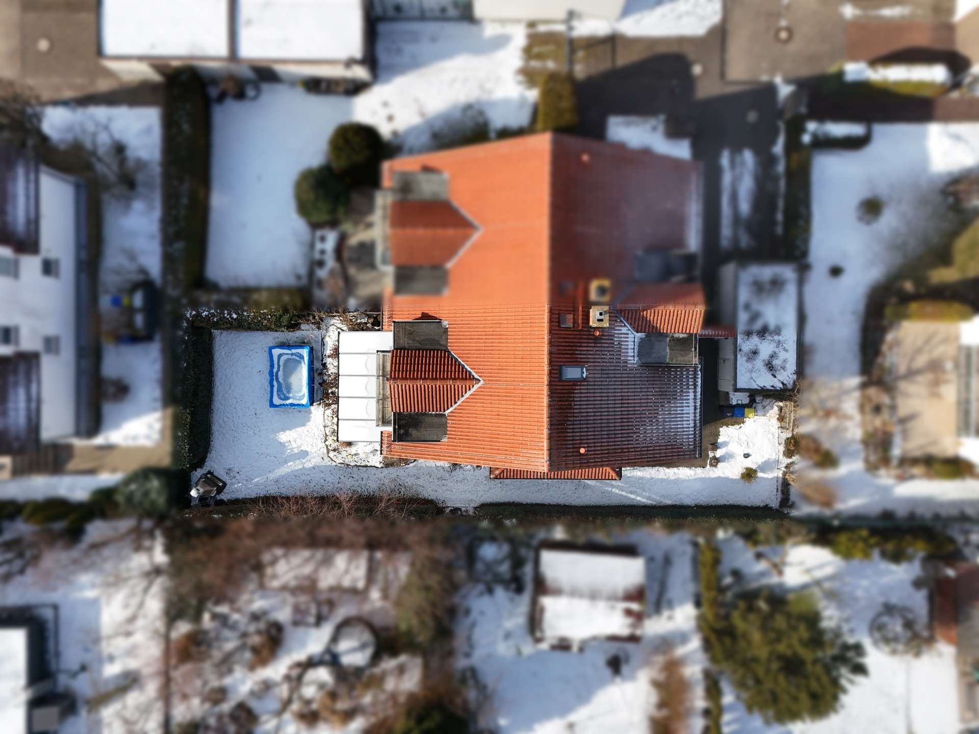Luftaufnahme eines Hauses mit rotem Dach, umgeben von Schnee und einem kleinen Pool im Garten.