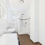 Modernes Badezimmer mit Dusche, Waschbecken und Handtuchheizkörper, hell und gut beleuchtet.