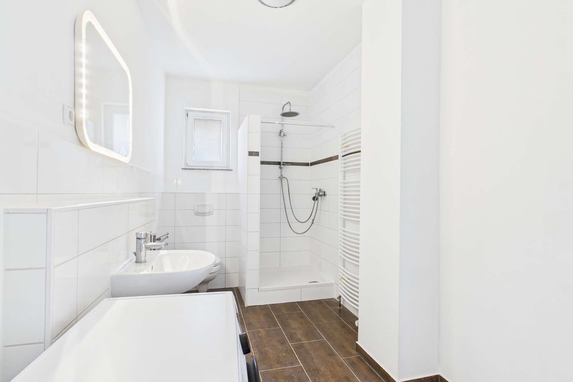 Modernes Badezimmer mit Dusche, Waschbecken und Handtuchheizkörper, hell und gut beleuchtet.
