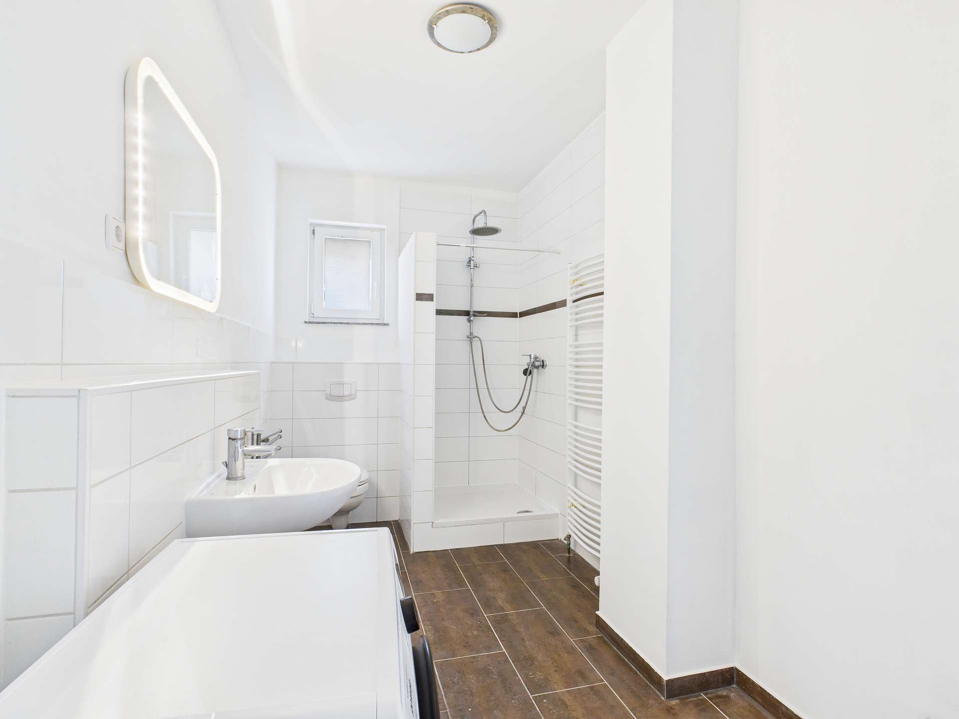 Modernes Badezimmer mit Dusche, Waschbecken und Handtuchheizkörper, hell und gut beleuchtet.