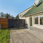Hinterhof mit Pflastersteinen, Gartenmöbeln und einer Wand aus Sichtschutz, umgeben von einer grünen Wiese.