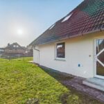 Ein einseitig belichtetes Wohnhaus mit grünem Rasen und angrenzendem Weg, unter einem klaren Himmel.