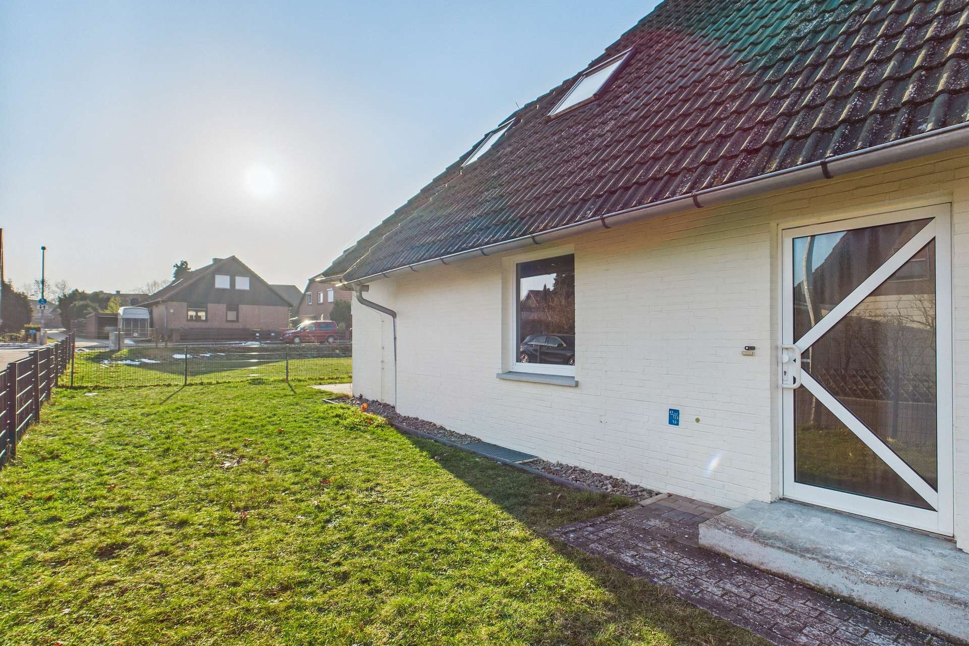 Ein einseitig belichtetes Wohnhaus mit grünem Rasen und angrenzendem Weg, unter einem klaren Himmel.