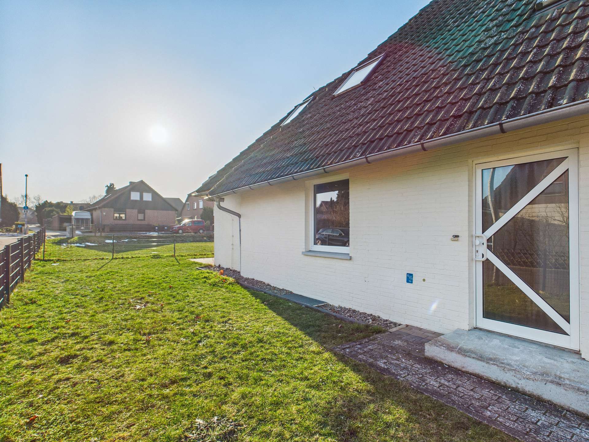 Ein einseitig belichtetes Wohnhaus mit grünem Rasen und angrenzendem Weg, unter einem klaren Himmel.