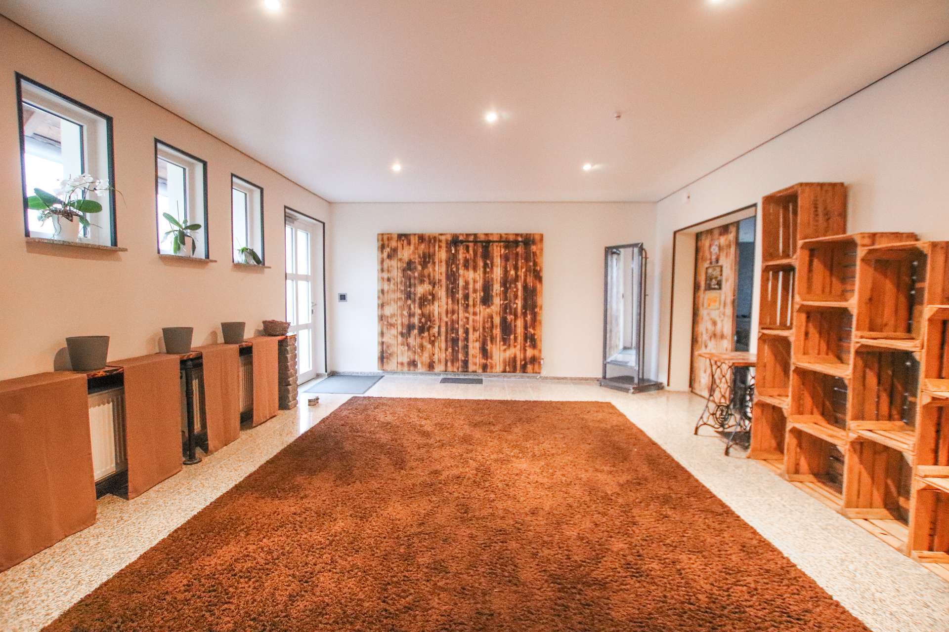 Geräumiger Eingangsbereich mit braunem Teppich, Holzregalen und rustikaler Wandschiebe. Helle Fenster sorgen für Licht.