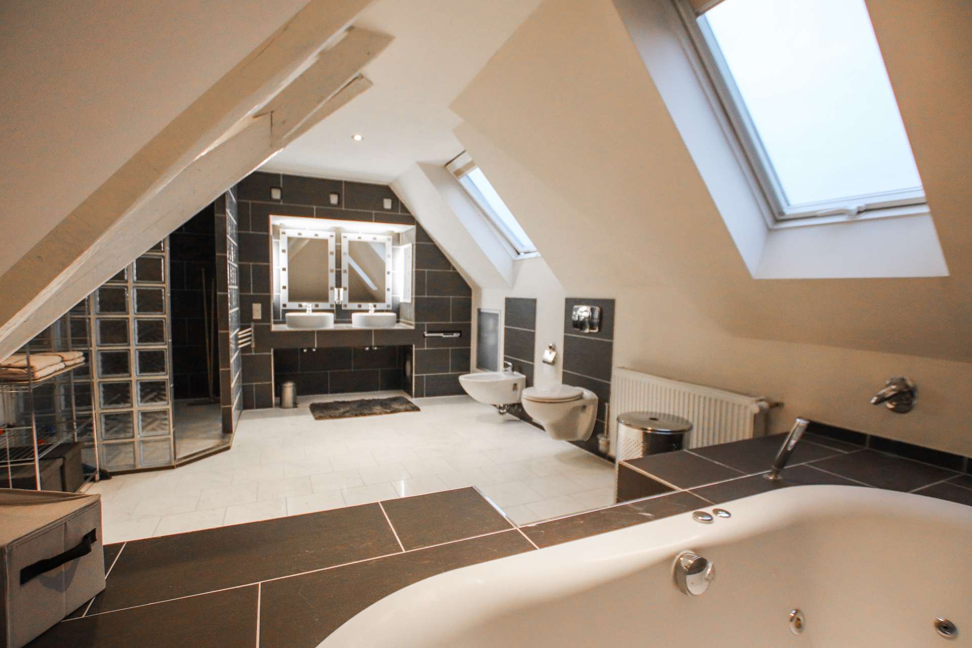 Modernes Badezimmer mit Dachfenstern, freistehender Badewanne, Doppelwaschbecken und eleganten Fliesen.