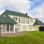 Ein modernes, zweigeschossiges Haus mit grünem Dach, großen Fenstern und einer gepflegten Rasenfläche im Hintergrund.