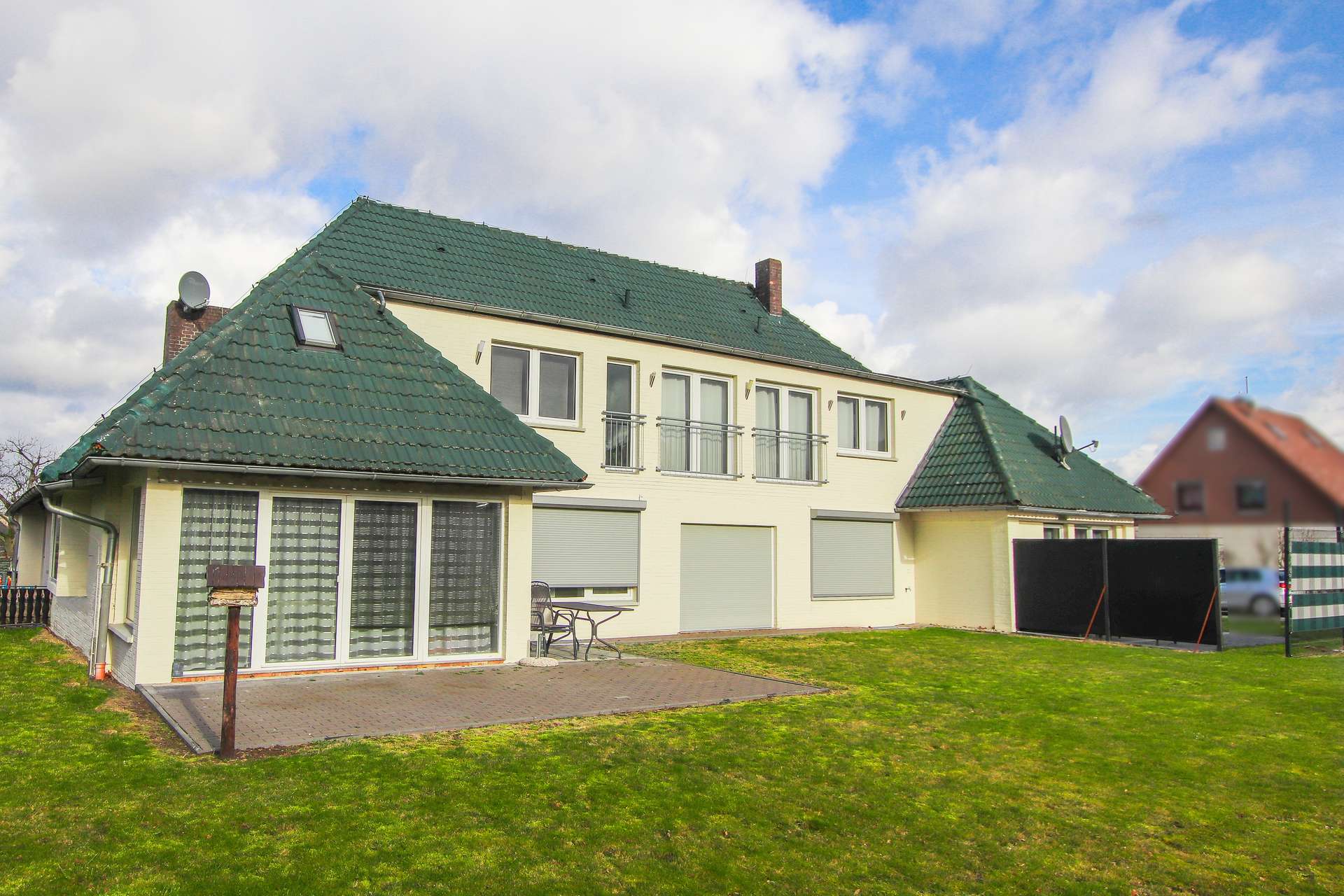 Ein modernes, zweigeschossiges Haus mit grünem Dach, großen Fenstern und einer gepflegten Rasenfläche im Hintergrund.