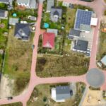 Luftaufnahme eines Wohngebiets mit Häusern, Straßen und einem unbebauten Grundstück in der Mitte.