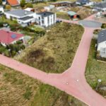 Luftaufnahme einer Wohngegend mit einer unbebauten Fläche und roten Straßen, umgeben von Wohnhäusern.