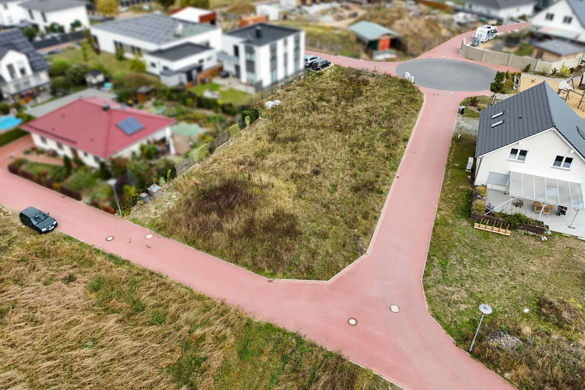 Luftaufnahme einer Wohngegend mit einer unbebauten Fläche und roten Straßen, umgeben von Wohnhäusern.