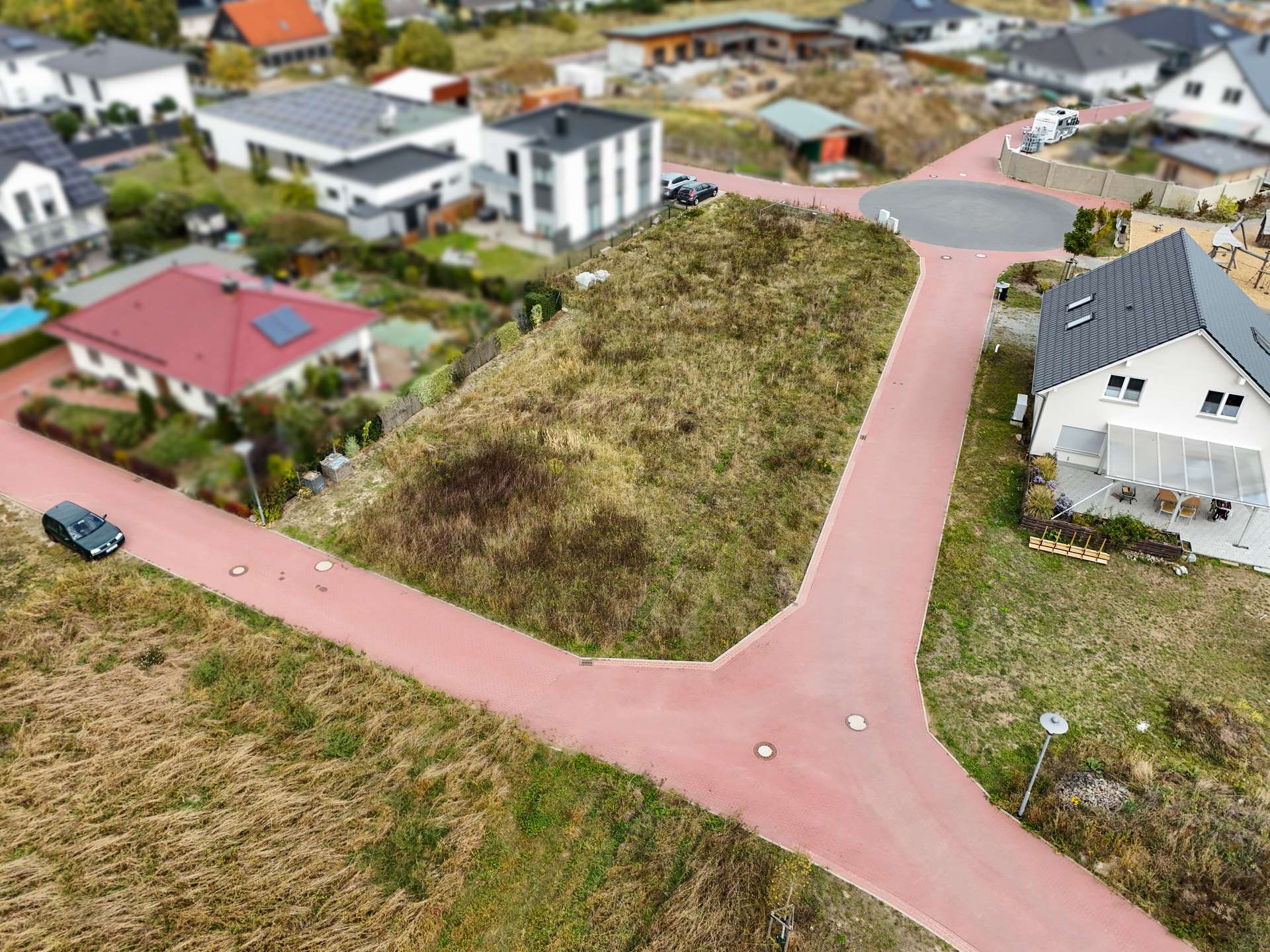Luftaufnahme einer Wohngegend mit einer unbebauten Fläche und roten Straßen, umgeben von Wohnhäusern.
