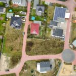Luftaufnahme eines Wohngebiets mit Einfamilienhäusern, Straßen und unbebautem Grundstück.