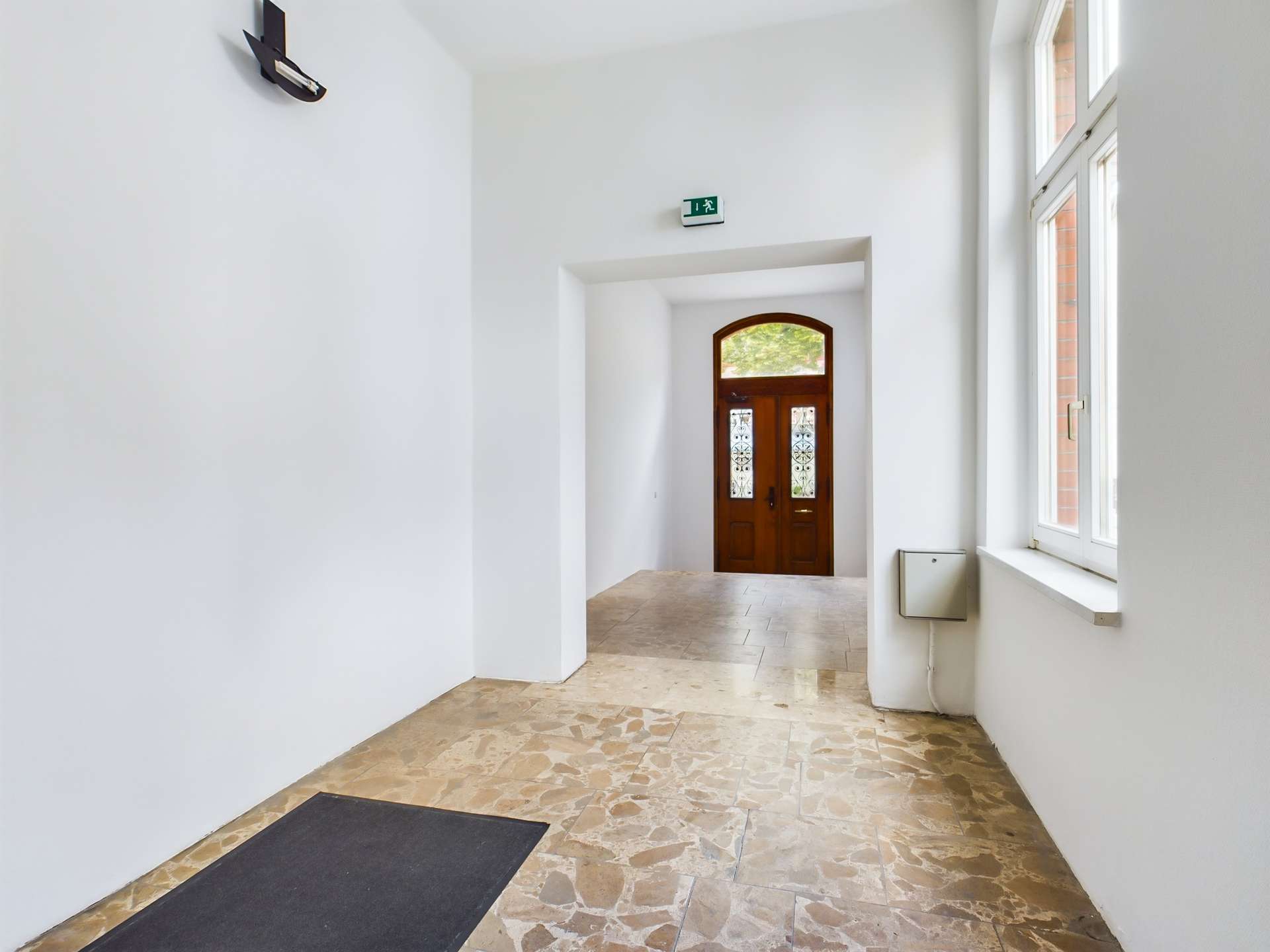 Heller Flur mit marmoriertem Boden und einer Tür aus Holz im Hintergrund, die ins Freie führt.