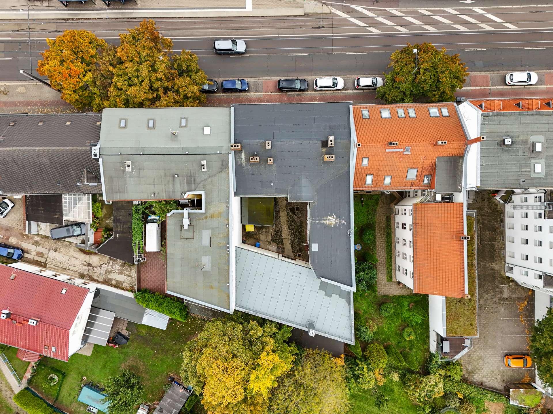 Luftaufnahme von Wohngebäuden mit unterschiedlichen Dächern und umgebenden Gärten in einer städtischen Umgebung.