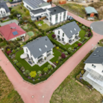Luftaufnahme von zwei modernen Häusern mit Gärten, umgeben von Straßen und weiteren Wohngebäuden.