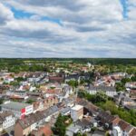 Luftaufnahme einer Stadt mit HĂ€usern, grĂŒnen FlĂ€chen und bewölktem Himmel.