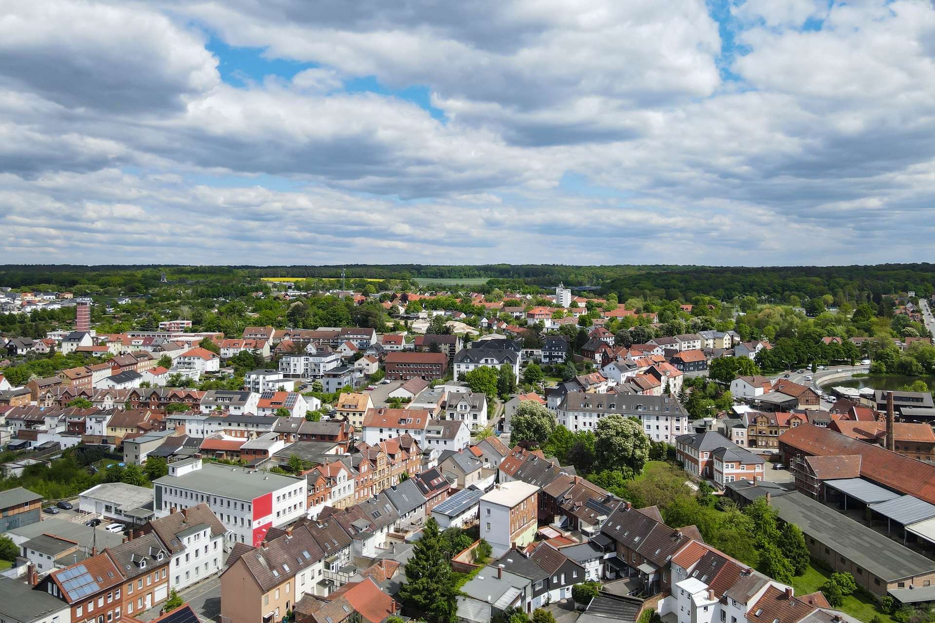 Luftaufnahme einer Stadt mit HĂ€usern, grĂŒnen FlĂ€chen und bewölktem Himmel.