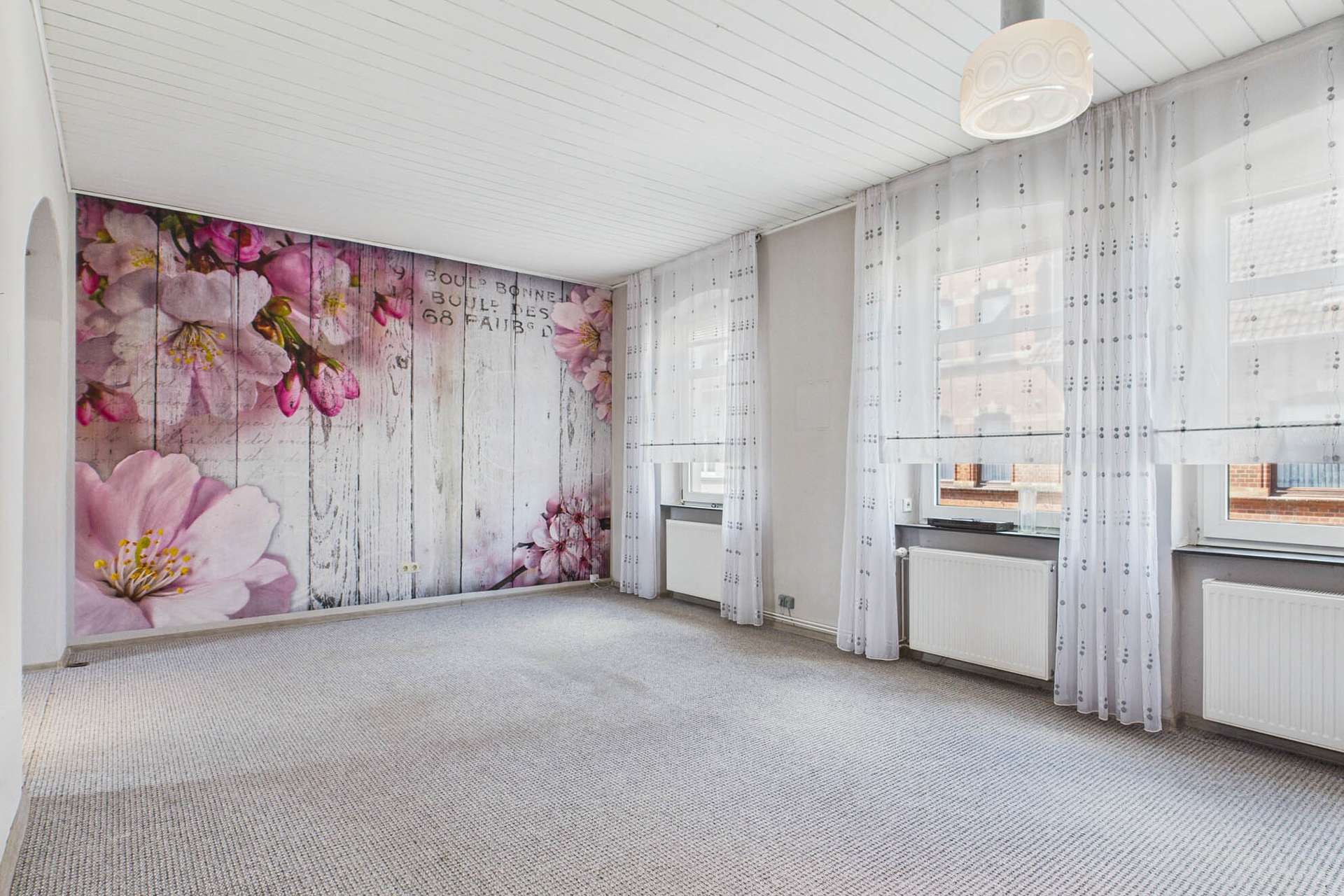 Heller Raum mit blĂŒtenverziertem Wanddesign und groĂen Fenstern, die Tageslicht hereinlassen.