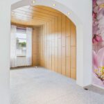 Heller Raum mit HolzvertÀfelung, Fenster mit VorhÀngen und einer Wanddekoration aus Blumenmotiven.