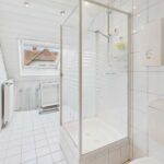 Badezimmer mit Duschkabine, WC und Fenstern, gefliest mit weiĂen Fliesen und hellen WĂ€nden.