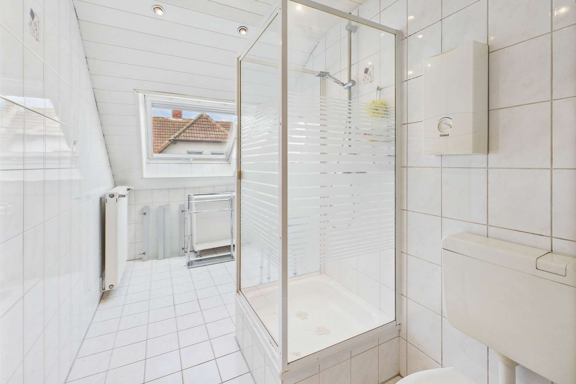 Badezimmer mit Duschkabine, WC und Fenstern, gefliest mit weiĂen Fliesen und hellen WĂ€nden.