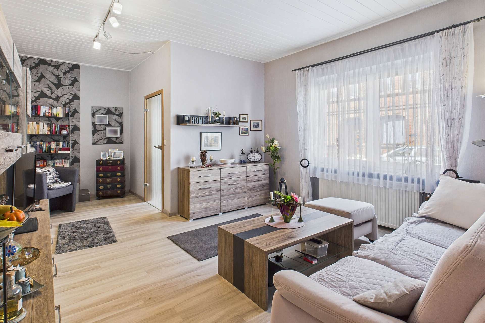 Helles Wohnzimmer mit Sofa, Couchtisch, Bücherregal und dekorativen Elementen an den Wänden.